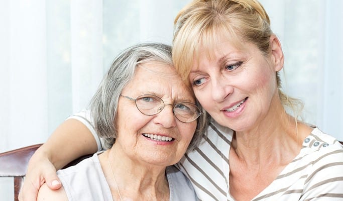 woman with half smile has arm around senior mom