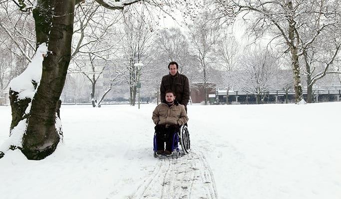 man helping someone in wheelchair through snow