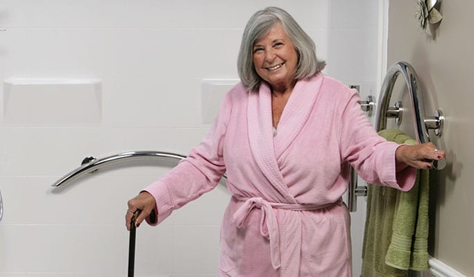 Senior women in pink robe holding chrome designer grab bar in bathroom