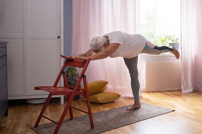 Senior woman in activewear exercising with chair and yoga mat