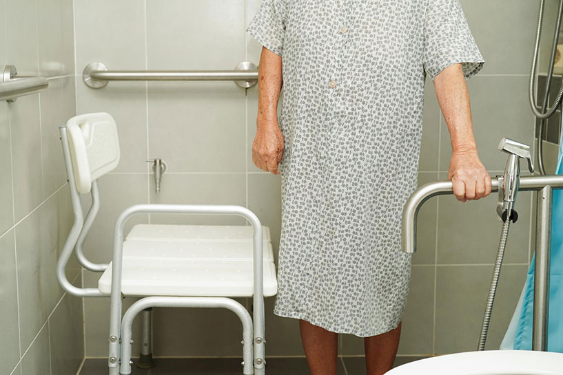 Senior woman holding on to grab rail and standing next to shower chair