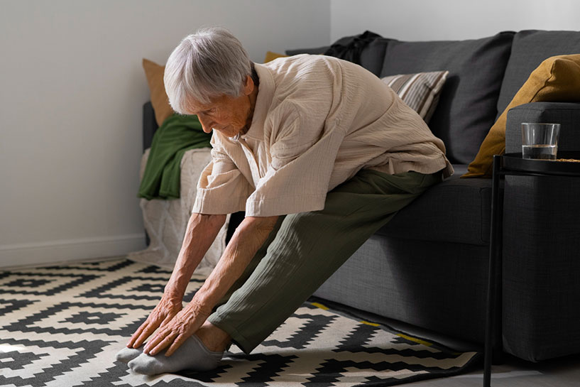 Senior woman sitting on couch and stretching her legs while bending her upper body