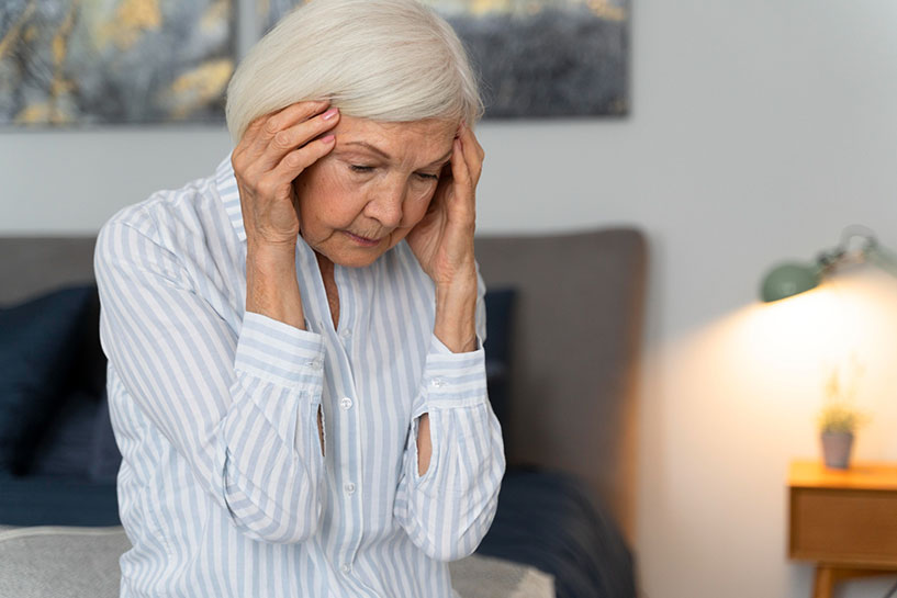 Senior woman sitting down & holding forehead due to dizziness