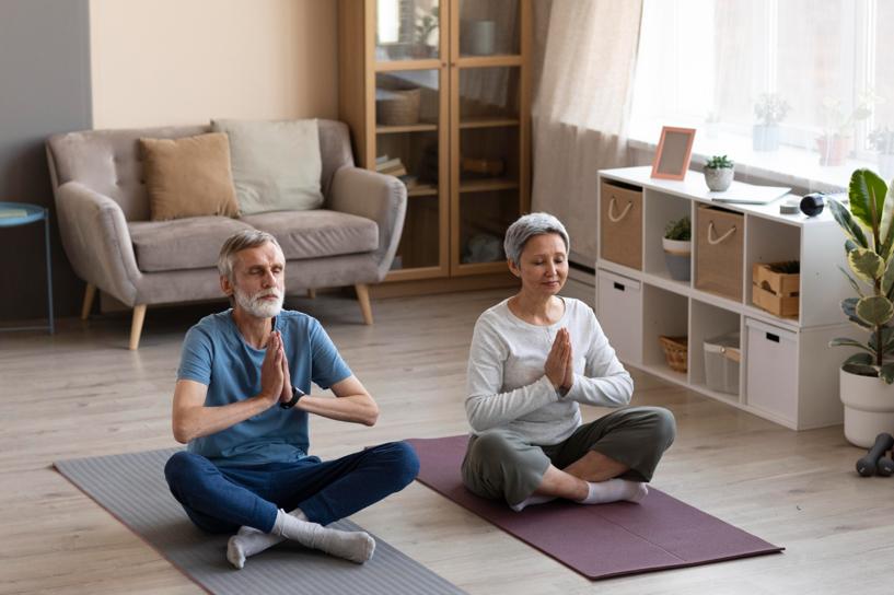 Senior couple sitting on yoga mats at home in yoga pose