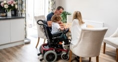 child in wheelchair with family at the table